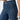 Woman wearing wide-leg high-waisted jeans paired with a neutral blazer, standing with one hand in pocket against a light background, showcasing casual chic style.