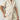 Women's beige high-waisted summer shorts made of lightweight textured cotton, modeled by a woman in a white dress shirt, showcasing the shorts' fit around the waist and legs.