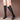 Women's black knee-high leather boots featuring a tassel and block heel, shown on a leg.
