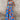 A woman wearing a blue floral wide-leg jumpsuit with short sleeves and a relaxed fit, perfect for resort fashion. The jumpsuit features a flattering waistline and a stylish neckline, complemented by the wearer's shoulder-length hairstyle.
