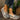 Women's brown wedge loafers styled as casual sneakers, worn on a person's feet standing on grass. The shoes feature a subtle pattern and embellishments, creating a stylish look.