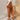 Women's high-waisted terracotta corduroy cropped pants worn by a model, showcasing the pants' fit around the waist and thighs, with the hem falling above the ankles. The model is paired with a blazer and dress shirt, emphasizing a chic and stylish outfit.