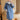 A woman wearing a light blue denim overshirt with a fleece lining, designed in a loose fit style. The overshirt features long sleeves and is worn as outerwear. She is standing, showcasing the garment's relaxed fit at the shoulders, waist, and overall structure.