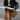 A woman wearing an oversized black leather jacket styled for casual street fashion, with visible details of the jacket's sleeves, waist, and open collar, standing against a plain backdrop.