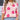 Women's pink floral crewneck sweater worn by a model. The sweater features a trendy autumn knitwear design with floral patterns. The model is accessorized with sunglasses and has shoulder-length hair, showcasing the sweater's stylish appearance.