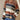 A woman wearing a multicolor striped crew neck sweater paired with jeans. The sweater features a mix of vibrant fall colors with a knit texture, showcasing a casual yet stylish look.