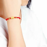 A close-up of a person wearing a 24K Gold Red String Bracelet with 3D Pixiu Beads and a 999 Gold Stamp on their wrist.