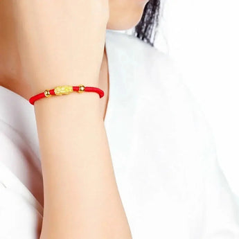 A close-up of a person wearing a 24K Gold Red String Bracelet with 3D Pixiu Beads and a 999 Gold Stamp on their wrist.