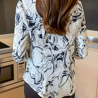 Abstract print beige and navy women's blouse featuring a swirl pattern. This office shirt highlights a structured design with attention to the shoulder and sleeve detailing, suitable for a professional setting. The blouse is worn by a standing model, showcasing its fit and overall style.