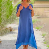 Asymmetrical blue V-neck maxi dress with side buttons, featuring a flowy design and short sleeves, displayed outdoors against a grassy background.