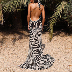 Backless zebra print maxi dress with a halter neck, worn by a woman standing outdoors among trees and grass.