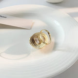 Baroque Pearl Statement Ring in luxury gold setting, showcased on a reflective surface with elegant dishware and serveware in the background.