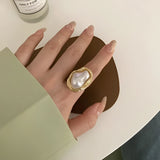 A luxurious gold cocktail ring featuring a large baroque pearl, worn on a woman's finger.