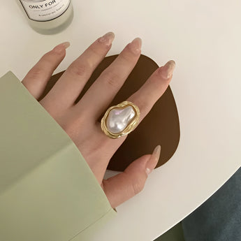 A luxurious gold cocktail ring featuring a large baroque pearl, worn on a woman's finger.