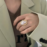 A woman's hand wearing a Baroque Pearl Statement Ring in luxury gold, positioned elegantly with a beige dress shirt sleeve visible in the background.