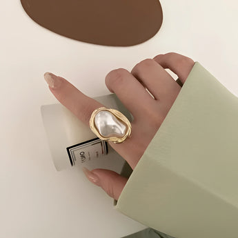 A luxurious gold cocktail ring for women featuring a large baroque pearl, worn on a hand with well-manicured nails.
