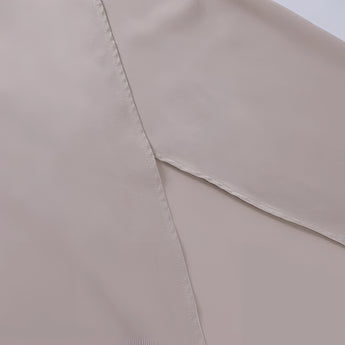 Beige cami top with adjustable straps, featuring a zipper detail, displayed on a wooden surface with a subtle pattern in the background.