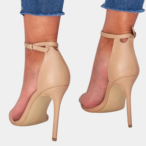 Beige ankle strap stiletto heels on a model showcasing elegant platform design with a focus on the footwear against a plain backdrop.