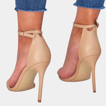 Beige ankle strap stiletto heels on a model showcasing elegant platform design with a focus on the footwear against a plain backdrop.