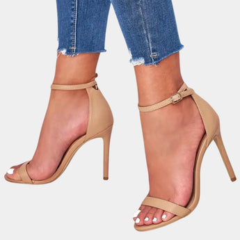 Beige ankle strap stiletto heels with an elegant platform, worn on a human leg, showcasing a fashionable and stylish footwear choice.