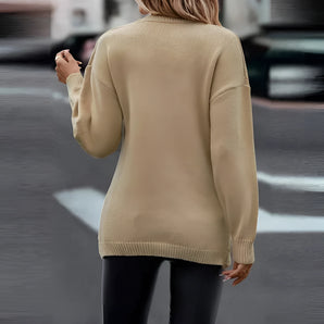 Woman wearing a beige crew neck sweater with long sleeves, styled as a casual fall fashion pullover. She is standing and has long hair, possibly wearing eyewear. The sweater is designed for women's fashion, highlighting the neckline and shoulder area.