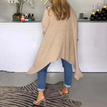 
A beige knit oversized cardigan for women's fall fashion is displayed, showcasing its long sleeves and loose fit. The cardigan is worn by a model standing indoors on wooden flooring, highlighting its cozy and stylish appeal.
