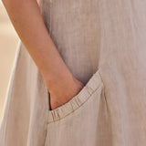 Beige linen dress with short sleeves and pockets, showcasing eco-friendly summer fashion. The dress features a comfortable fit, with a focus on the shoulder, neck, and waist areas against a wooden backdrop.