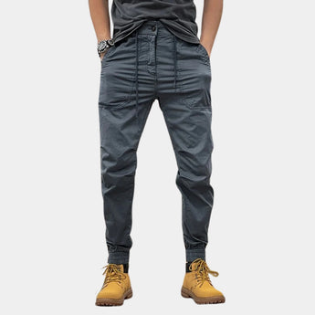 Dark gray men's slim fit cargo pants featuring multiple pockets, designed for outdoor wear, shown in a 3XL size. The pants are styled with a focus on durability and fashion, emphasizing the thigh and waist areas.