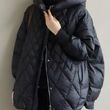 A black oversized hooded puffer jacket designed as a lightweight winter coat, featuring long sleeves and a high collar. The jacket is modeled on a person with visible shoulder and waist detailing, showcasing its fashionable and cozy fit suitable for winter. The image is captured with flash photography, highlighting the jacket's sleek design.