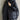 A black oversized hooded puffer jacket designed as a lightweight winter coat, featuring long sleeves and a high collar. The jacket is modeled on a person with visible shoulder and waist detailing, showcasing its fashionable and cozy fit suitable for winter. The image is captured with flash photography, highlighting the jacket's sleek design.