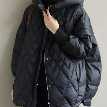 A black oversized hooded puffer jacket designed as a lightweight winter coat, featuring long sleeves and a high collar. The jacket is modeled on a person with visible shoulder and waist detailing, showcasing its fashionable and cozy fit suitable for winter. The image is captured with flash photography, highlighting the jacket's sleek design.