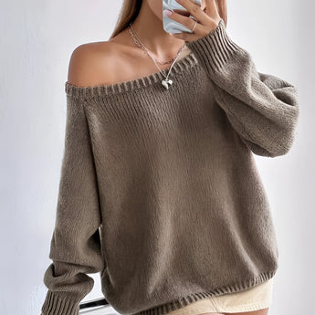 Beige oversized off-shoulder knit sweater worn by a person with long hair, showcasing trendy fall fashion. The sweater features loose-fitting sleeves and a relaxed fit, highlighting the individual's shoulders and arms.