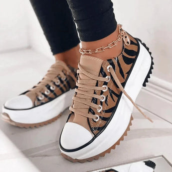 Beige platform sneakers with chunky sole and star heel detail, featuring a striped tiger design, worn by a woman in streetwear fashion.