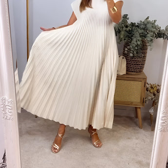 Beige pleated midi dress with pockets, featuring a sleeveless design. The dress is worn outdoors, showcasing the waist and arm details, with a backdrop of plants and a flowerpot.