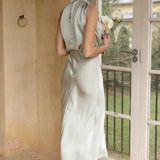 Beige sleeveless backless midi dress featuring an elegant design, ideal for weddings and cocktail events, displayed on a mannequin near a window with focus on the dress's neckline and waist.