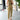 Beige sleeveless belted jumpsuit displayed on a mannequin with a focus on casual chic summer fashion, featuring a defined waist and flowing design, set against a backdrop with houseplants and a window.