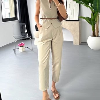 Beige sleeveless belted jumpsuit displayed on a hanger, featuring a chic summer design with a belt at the waist, set against a neutral background with a potted plant nearby.