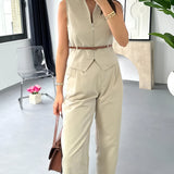 Beige sleeveless belted jumpsuit with a casual chic design, featuring a fitted waist and wide leg cut, displayed on a mannequin against a backdrop of window blinds.