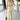 Beige sleeveless belted jumpsuit with a casual chic design, featuring a fitted waist and wide leg cut, displayed on a mannequin against a backdrop of window blinds.