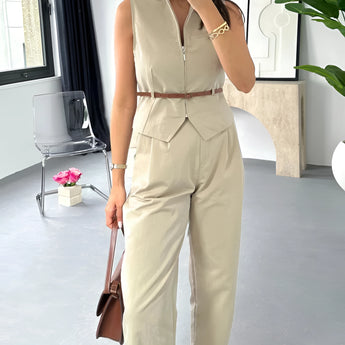 Beige sleeveless belted jumpsuit with a casual chic design, featuring a fitted waist and wide leg cut, displayed on a mannequin against a backdrop of window blinds.