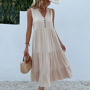 
A beige sleeveless midi dress with button-front design, worn by a model. The dress features a flowy summer style, highlighting the shoulders and waist. The model poses with an arm gesture, emphasizing the dress's elegant cut suitable for day wear. The apricot color of the dress in size XL is showcased, with no additional accessories visible.