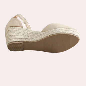 Beige suede espadrilles featuring a closed toe and wedge heel with an ankle strap, designed for outdoor wear as a fashionable walking shoe.