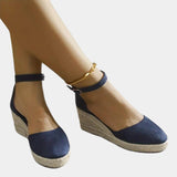 Marine blue suede espadrilles with a closed toe and ankle strap, featuring a wedge heel design, displayed on a human foot, highlighting the fashion-forward and elegant style of the footwear.