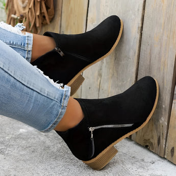 Beige suede women's ankle boots with a low heel and zipper, styled with black denim jeans.