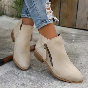 Beige suede women's ankle boots with a low heel and zipper, showcased on a model's legs.
