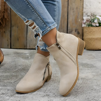 Beige suede women's ankle boots with a low heel and side zipper, displayed with a focus on the shoe's elegant design and texture.