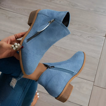 Beige suede women's ankle boots with a low heel and zipper, shown in a denim blue color variant, styled on a model's foot against a background that highlights the boots' elegant design and texture.