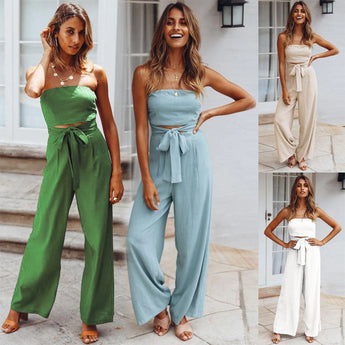 Beige sleeveless jumpsuit with a tie waist, modeled on a smiling person with long hair. The outfit is styled elegantly for casual summer wear, with emphasis on the waist and shoulder design.