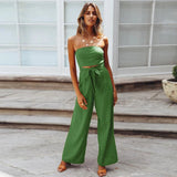 Beige sleeveless jumpsuit with a tie-waist, styled elegantly for casual summer wear, displayed on a mannequin with a flowerpot and green plant nearby, showcasing its fashionable design.