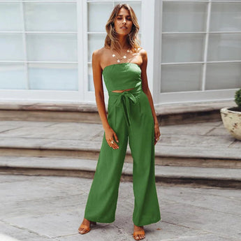 Beige sleeveless jumpsuit with a tie-waist, styled elegantly for casual summer wear, displayed on a mannequin with a flowerpot and green plant nearby, showcasing its fashionable design.